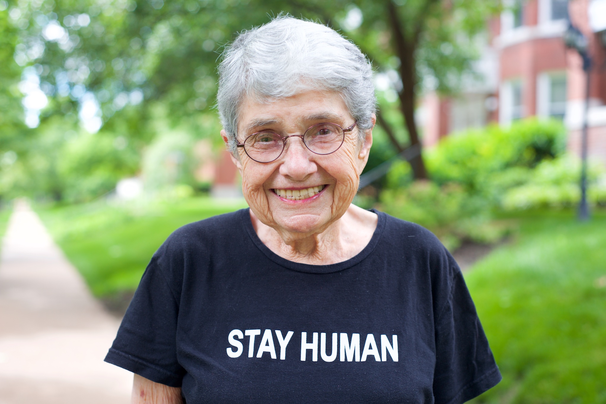 Hedy Epstein, woman in her 90s, faces the camera wearing a black T shirt with the words STAY HUMAN in white block letters.