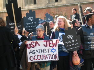 Hedy Epstein holding a sign "USA Jew Against Occupation" participating in a Women in Black Demonstration. Jerusalem, 2003