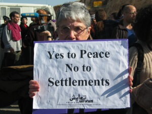 Hedy Epstein standing with a sign that says "Yes to Peace No to Settlements" during a demonstration against the occupation of Palestine.